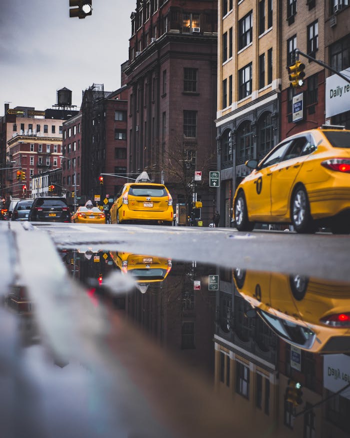 Vibrant city street with iconic yellow taxis, reflective puddles, and historic architecture.